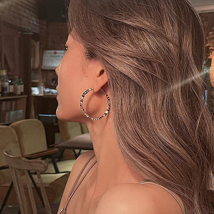 Frau mit großen, goldenen Creolen-Ohrringen in einem Café, stilvolle Modeaccessoires.
