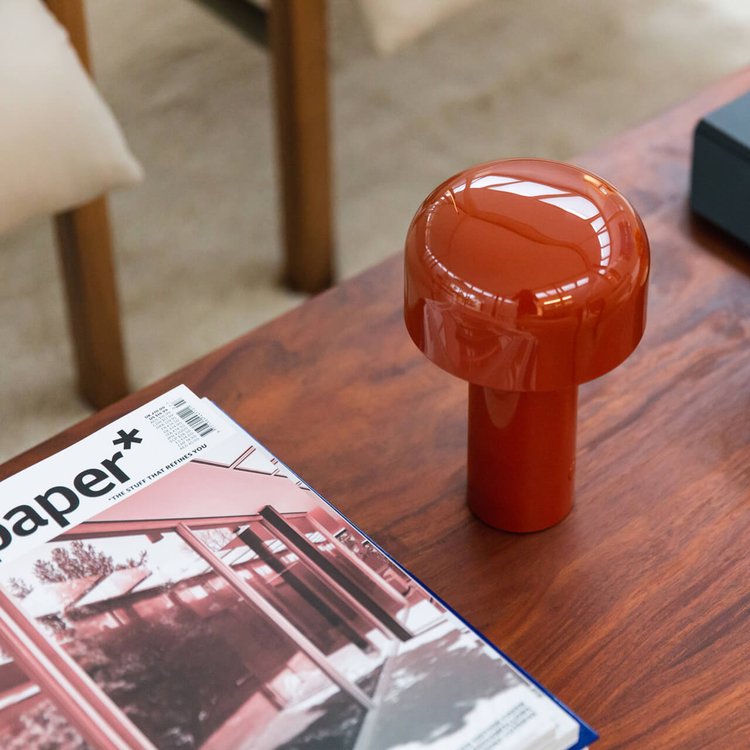 Rote Keramik-Tischlampe auf Holztisch neben Zeitschrift, modernes Innendesign.