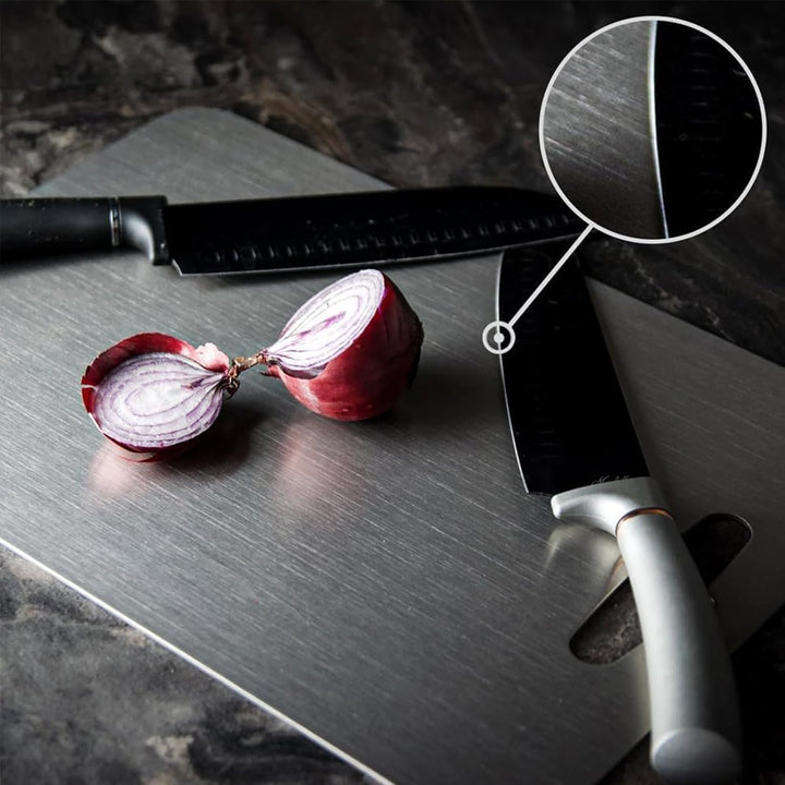 Zwei Küchenmesser auf Edelstahl-Schneidebrett mit halbierter roter Zwiebel, Nahaufnahme der Klinge.