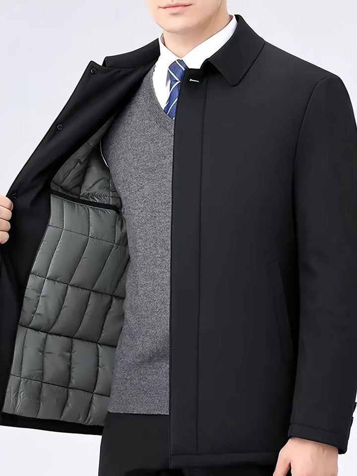 Mann in schwarzem Mantel mit grauem Innenfutter, grauem Pullover und blauer Krawatte.
