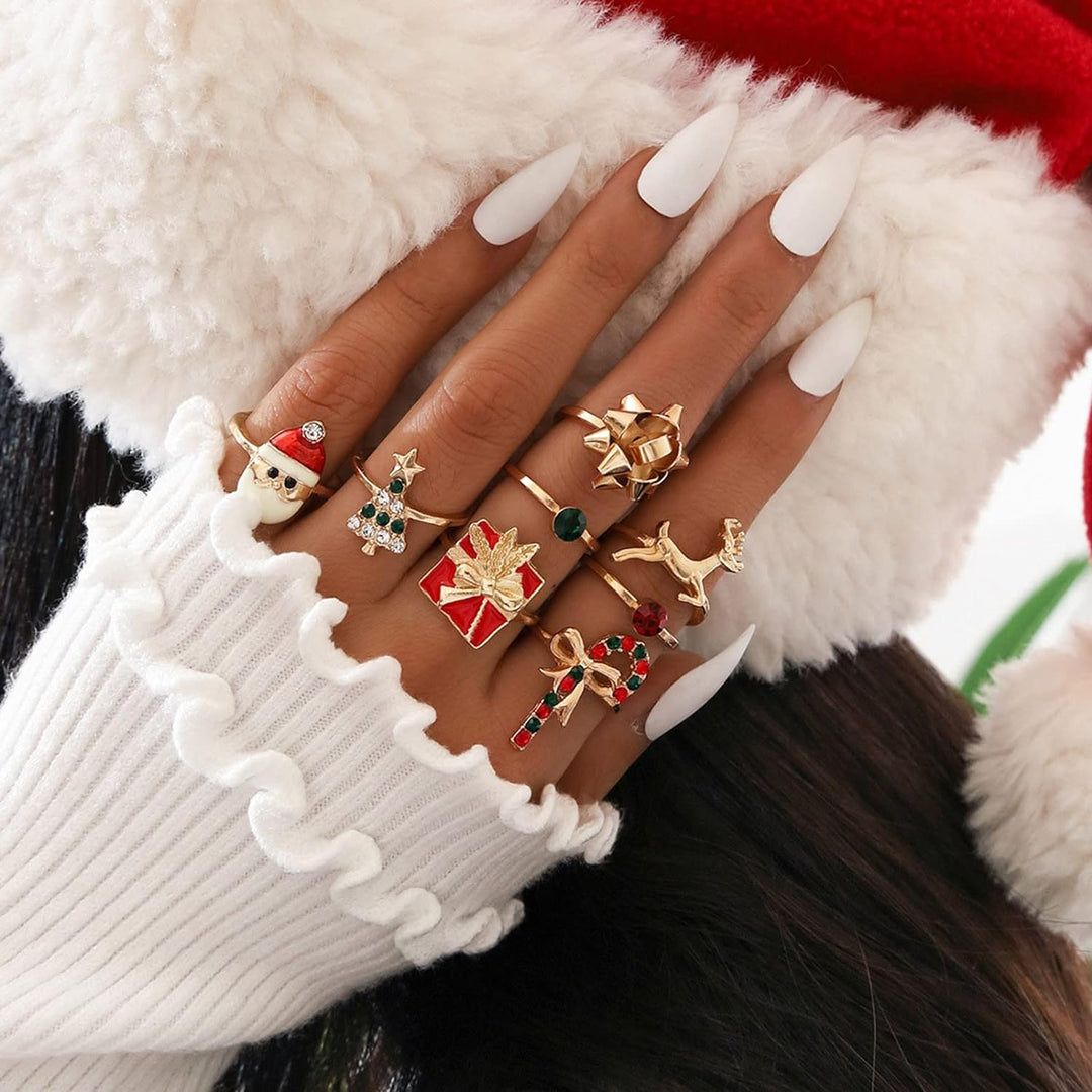 Damenhand mit Weihnachtsringen, goldfarben, festliche Motive, weiße Nägel, Pulloverärmel.