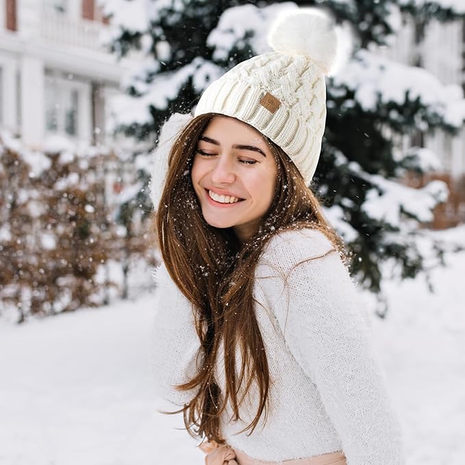 Frau mit weißer Strickmütze und Pompon im Schnee, Wintermode, lächelnd, draußen.