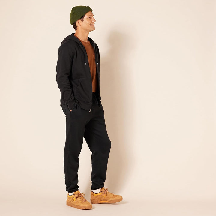 Mann in schwarzem Hoodie und Jogginghose, braune Sneaker, grüner Beanie, lässige Mode.