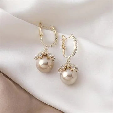 Goldene Ohrringe mit Perlenanhänger und Strasssteinen auf weißem Stoff, eleganter Schmuck.