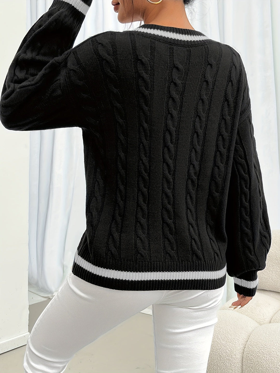 Frau trägt schwarzen Zopfmuster-Pullover, weiße Hose, modisch, elegant, Herbstmode.