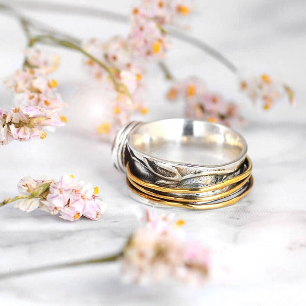 Silberring mit goldenen Akzenten, florales Design, auf Marmorhintergrund mit rosa Blüten.