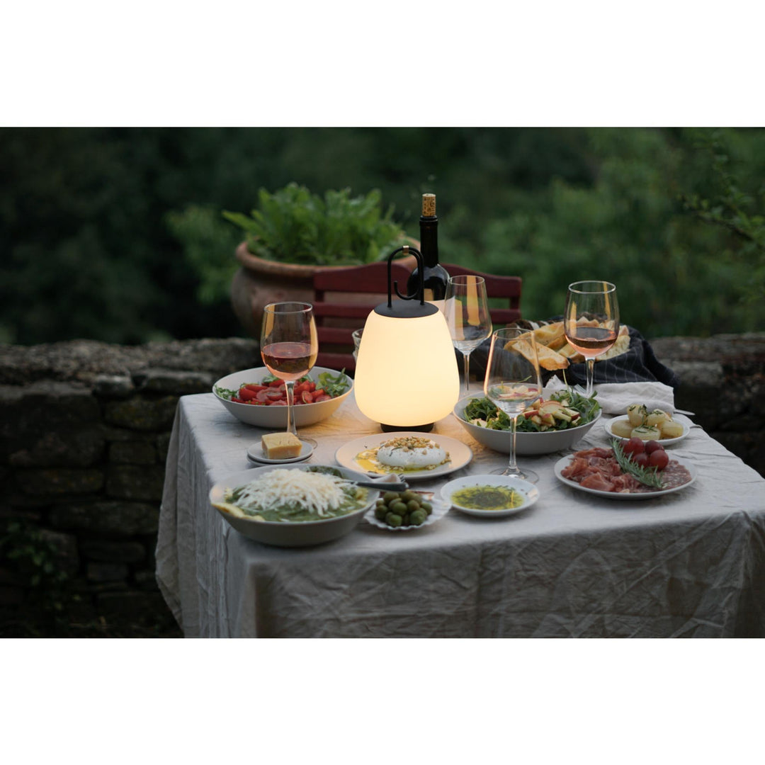 Tisch mit Speisen, Weingläsern und leuchtender Lampe im Freien, Abendessen im Garten.
