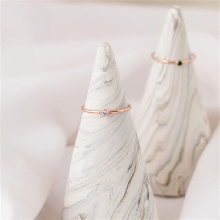 Zwei filigrane Ringe aus Roségold mit Edelsteinen auf marmorierten Kegeln präsentiert.