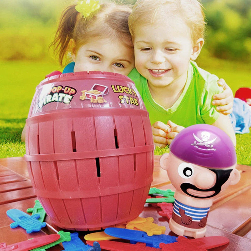 Zwei Kinder spielen mit Pop-Up-Piratenspiel, rotes Fass, bunte Schwerter, lila Piratenfigur.