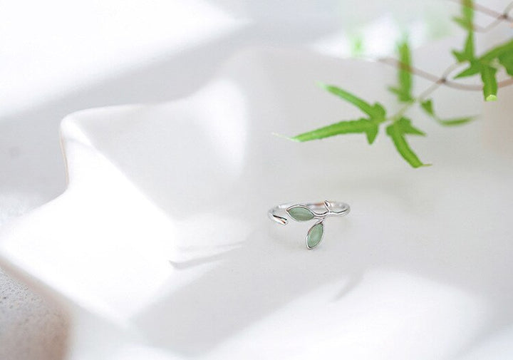 Silberner Ring mit grünen Blättern, verstellbar, auf weißem Keramikteller, Schmuckdesign.
