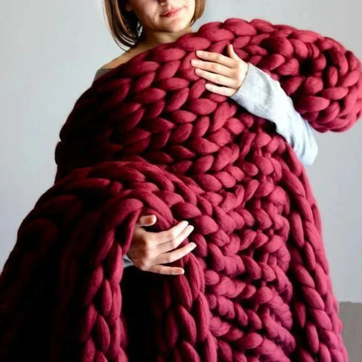 Frau mit großer, roter, grob gestrickter Decke aus Wolle, gemütlich und warm.