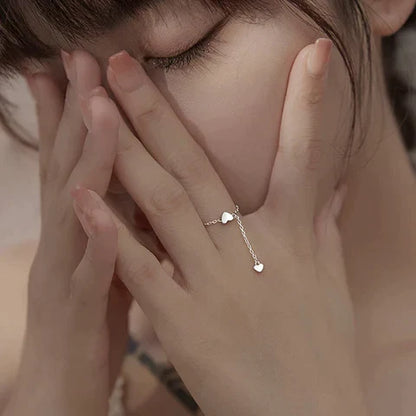 Frau mit silbernem Herzring, zartes Design, Schmuck, Modeaccessoire, eleganter Stil.