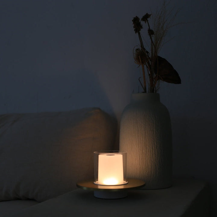 Moderne Tischlampe mit warmem Licht neben weißer Vase auf Sofa, minimalistische Wohnkultur.