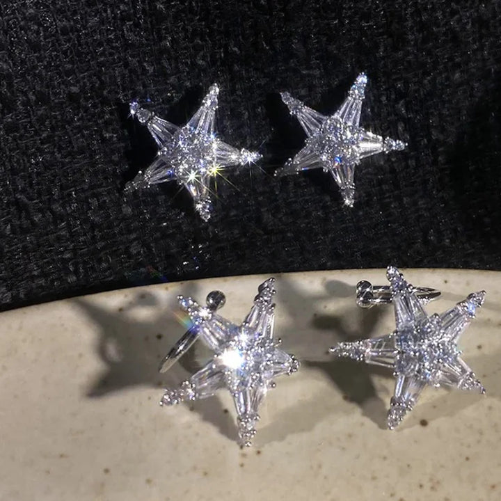 Sternförmige Ohrringe aus Silber mit funkelnden Kristallen auf schwarzem Hintergrund.