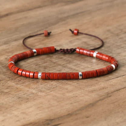 Rotes Perlenarmband aus Holz mit silbernen Akzenten auf Holztisch, verstellbar, handgefertigt.
