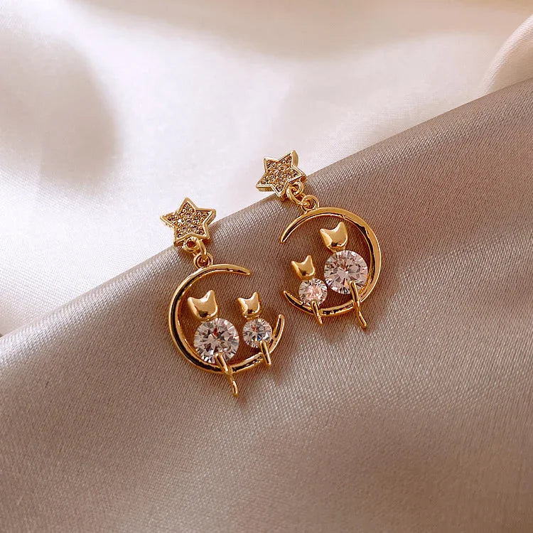 Goldene Ohrringe mit Stern- und Mondmotiv, Katzen-Design, funkelnde Kristalle, elegant, modisch.