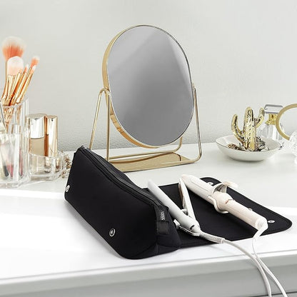 Schwarze Kosmetiktasche mit weißem Lockenstab auf Schminktisch, goldener Spiegel im Hintergrund.