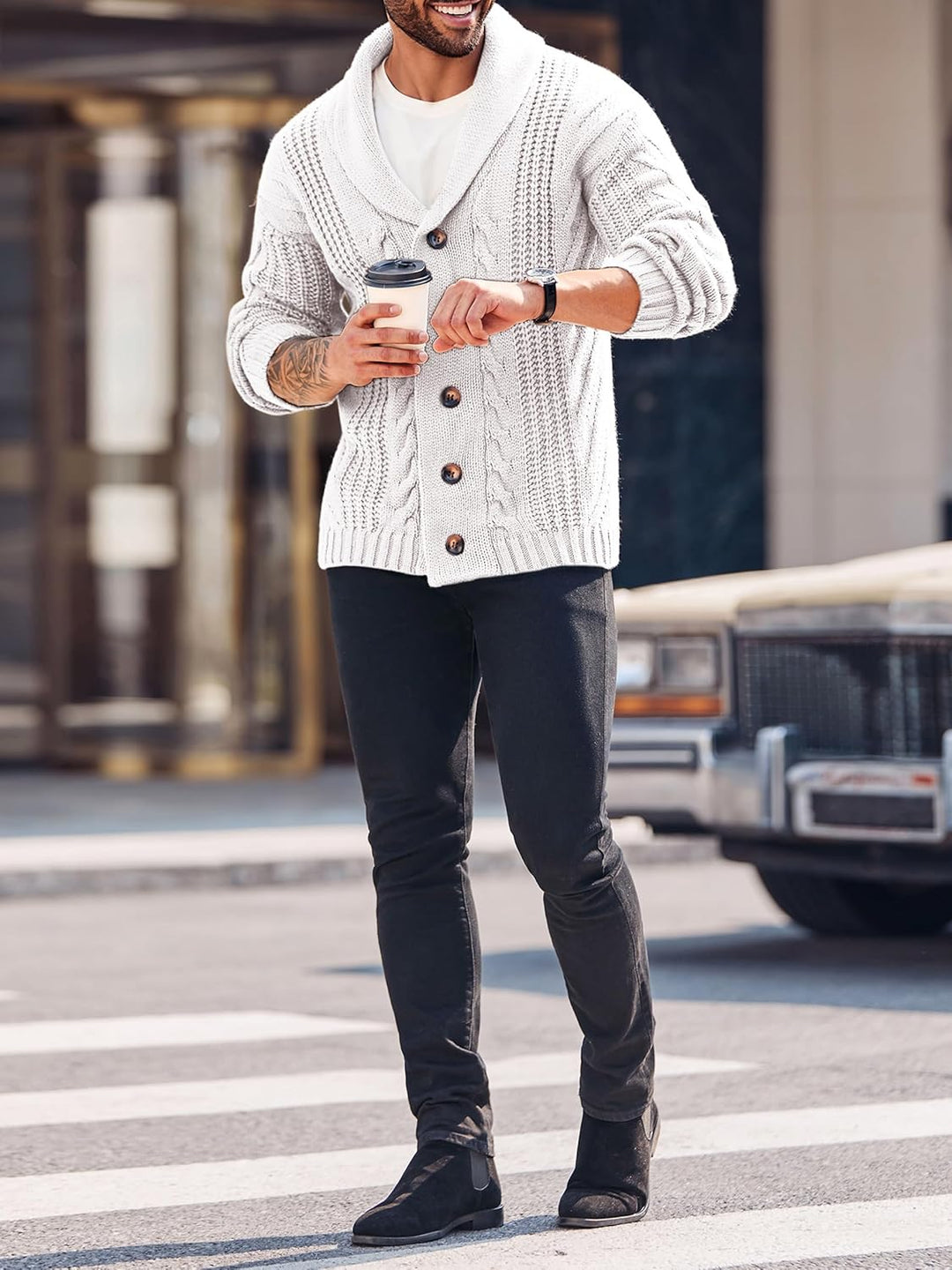 Mann in weißem Strickcardigan mit Kaffeebecher, schwarze Jeans, Straße, Herbstmode.