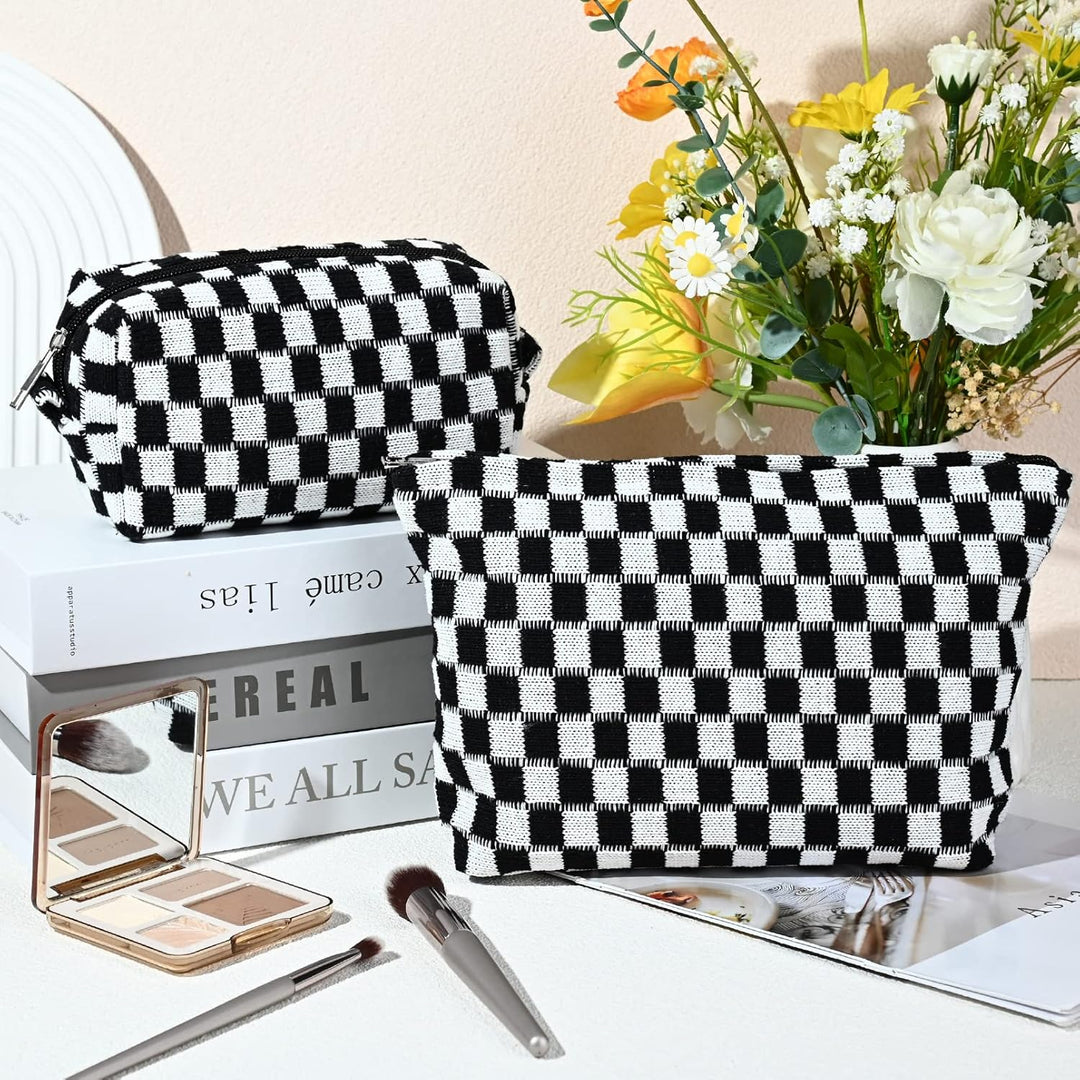 Schwarz-weiß karierte Kosmetiktaschen auf Büchern, mit Blumen und Make-up-Pinsel im Hintergrund.