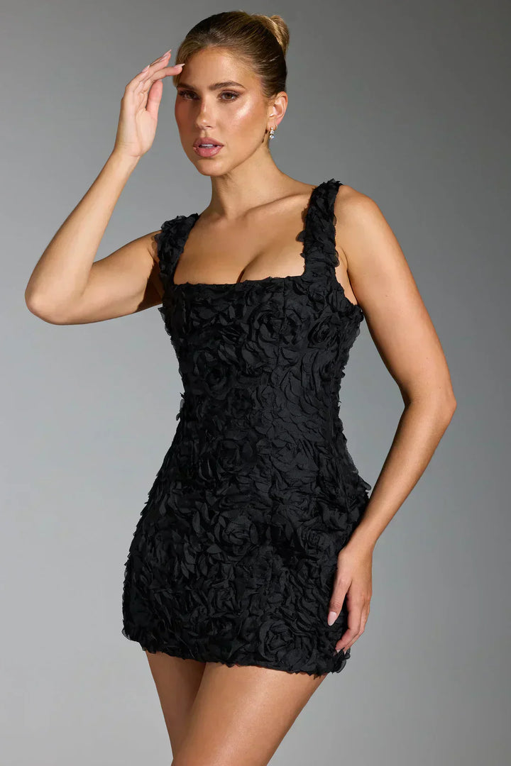 Frau in schwarzem, ärmellosem Minikleid mit Blumenmuster, elegantes Abendoutfit.