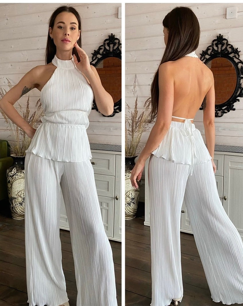 Frau in weißem, ärmellosem, plissiertem Jumpsuit mit offenem Rücken, elegantes Design.