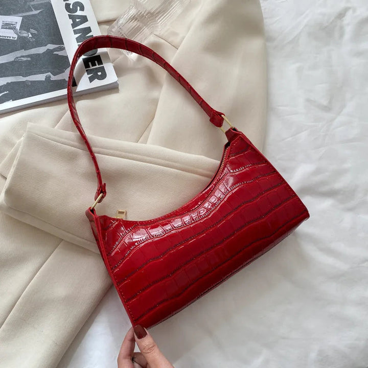 Rote Damenhandtasche aus Leder mit Krokodilprägung auf beigem Stoffhintergrund.
