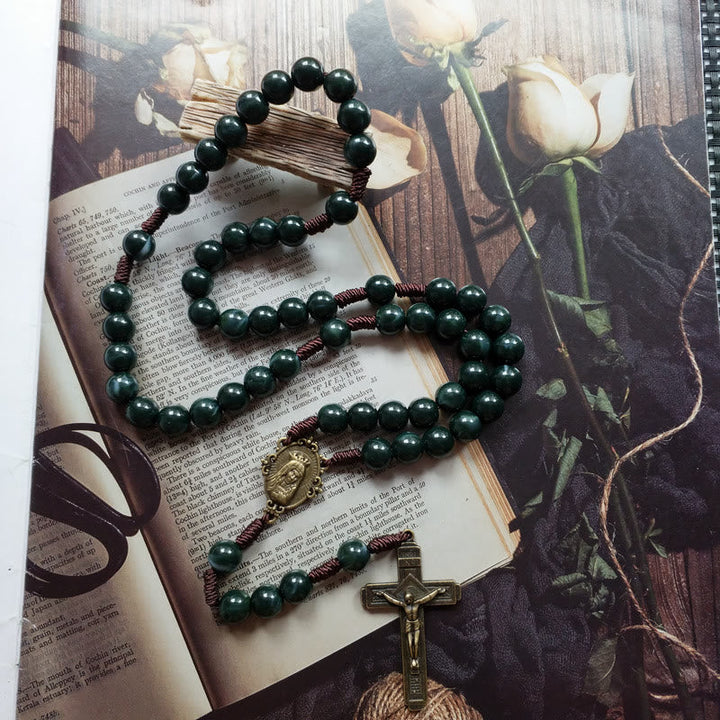 Rosenkranz mit grünen Perlen und Kreuz auf Buch und Rosenhintergrund, religiöses Schmuckstück.