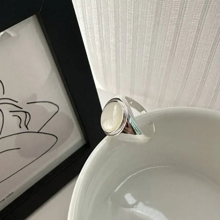 Silberring mit weißem Stein auf weißer Schale, minimalistisches Design, Schmuckfotografie.