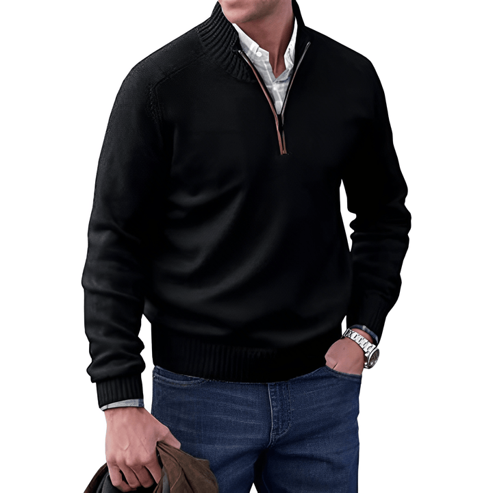 Mann in schwarzem Pullover mit Reißverschluss, weißem Hemd und blauer Jeans, hält braune Jacke.