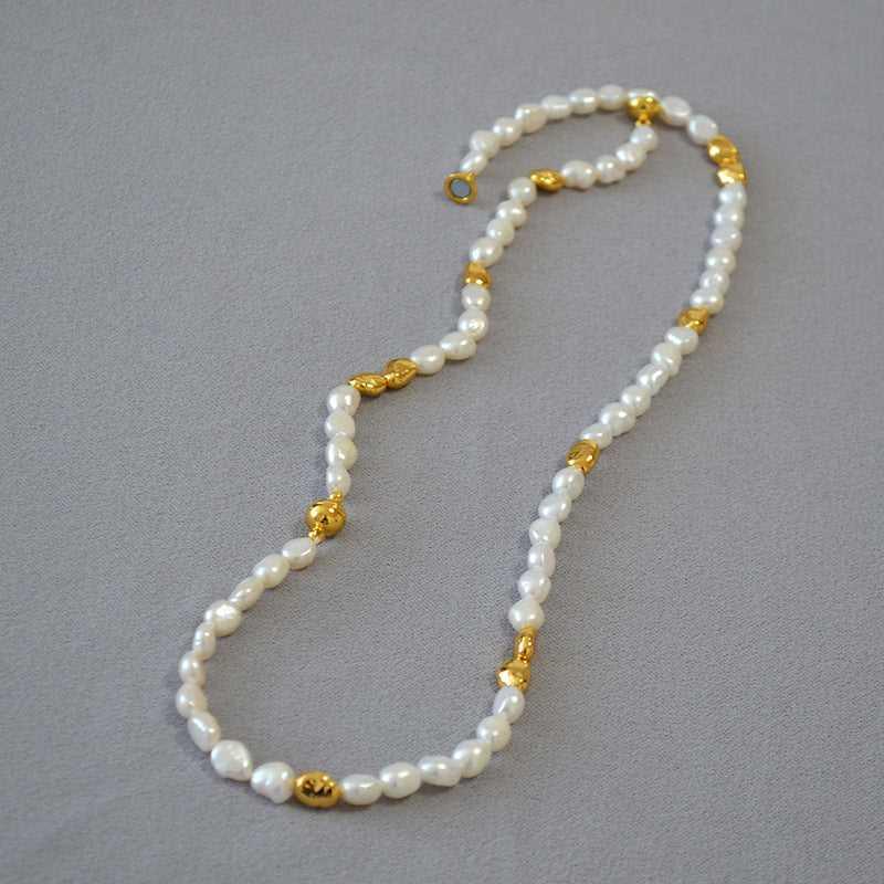 Perlenkette mit goldenen Zwischenelementen auf grauem Hintergrund, eleganter Schmuck, Damenaccessoire.