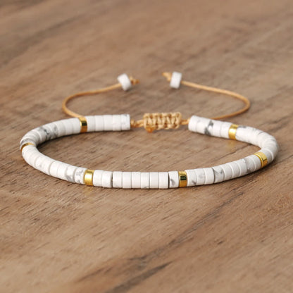 Armband aus weißen und goldenen Perlen, verstellbar, auf Holzoberfläche.