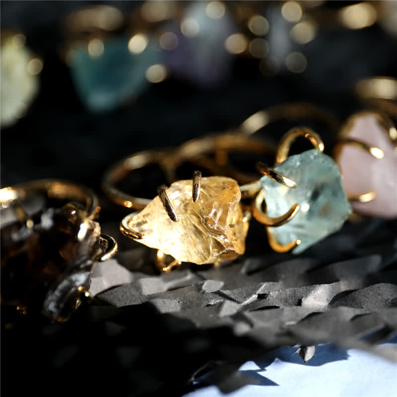 Goldene Ringe mit rohen Edelsteinen, Citrin und Aquamarin, auf schwarzem Hintergrund.