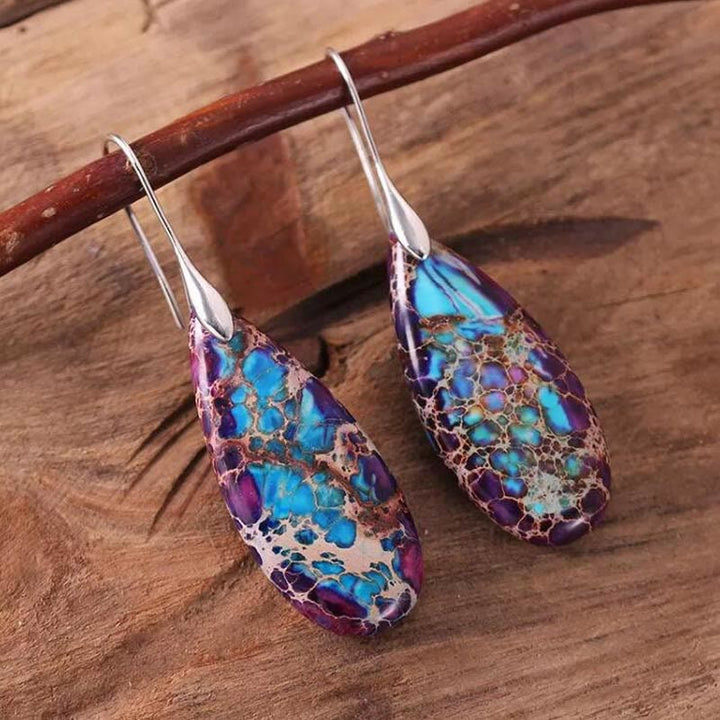 Bunte Tropfen-Ohrringe aus Harz und Metall auf Holzoberfläche, handgefertigter Schmuck.