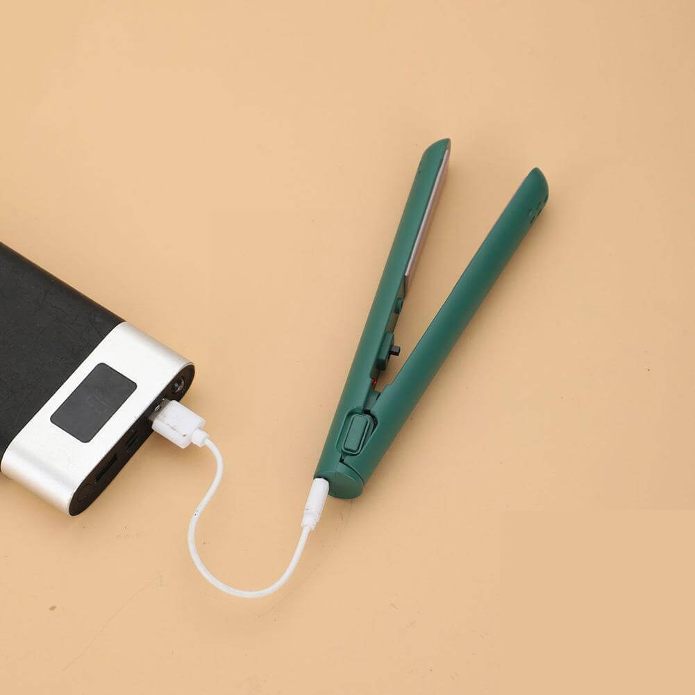 Zelená mini žehlička na vlasy otevřená na béžovém podkladu, napájená bílým USB kabelem z powerbanky s displejem. 11