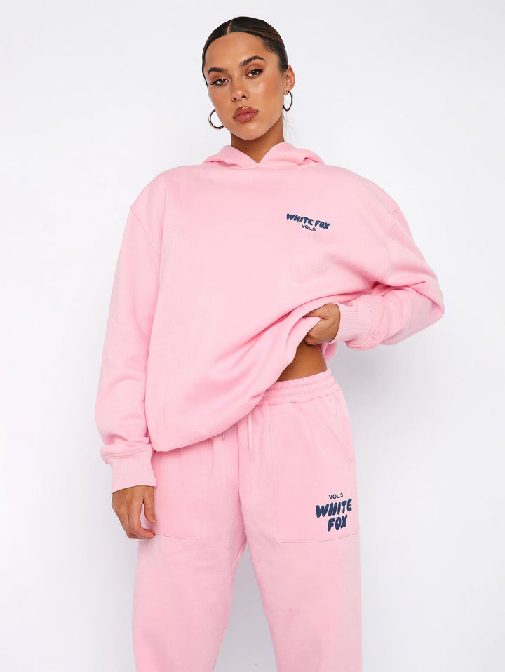 Frau in rosa Hoodie und Jogginghose, White Fox Logo, Freizeitmode, bequeme Damenbekleidung.