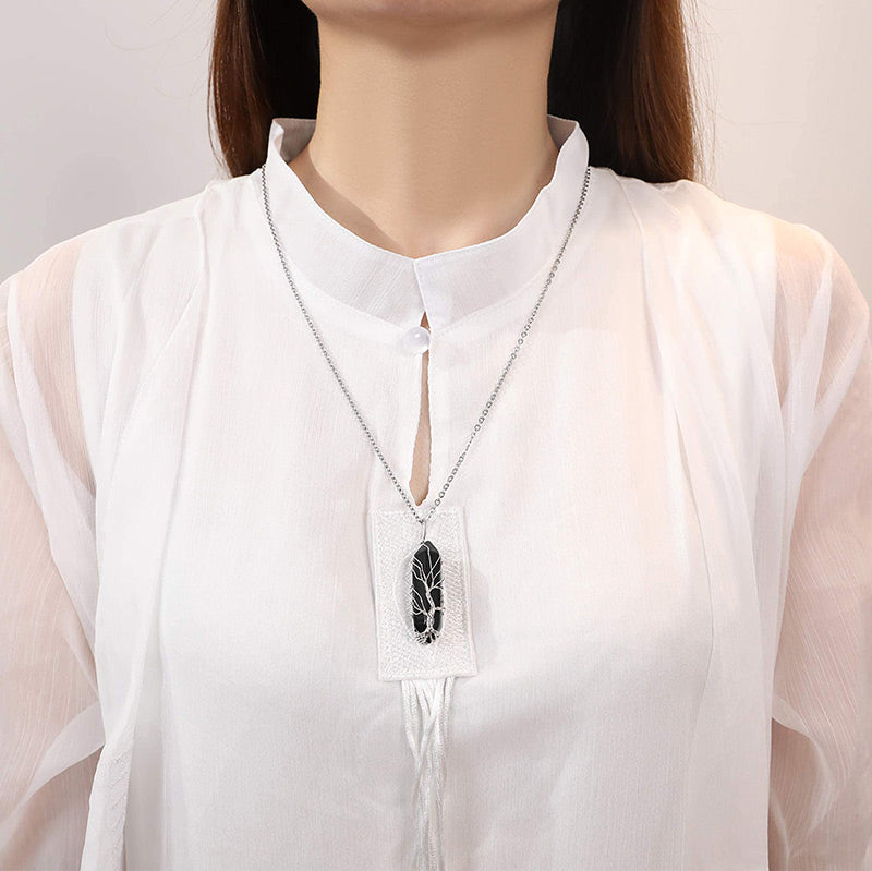 Frau mit weißer Bluse trägt silberne Halskette mit schwarzem Anhänger, eleganter Schmuck.