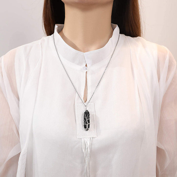 Frau mit weißer Bluse trägt silberne Halskette mit schwarzem Anhänger, eleganter Schmuck.