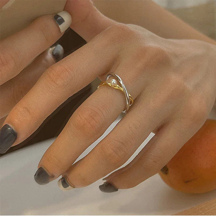 Damenhand mit silbernem und goldenem Ring, Perlendetail, stilvoller Schmuck, Nahaufnahme.