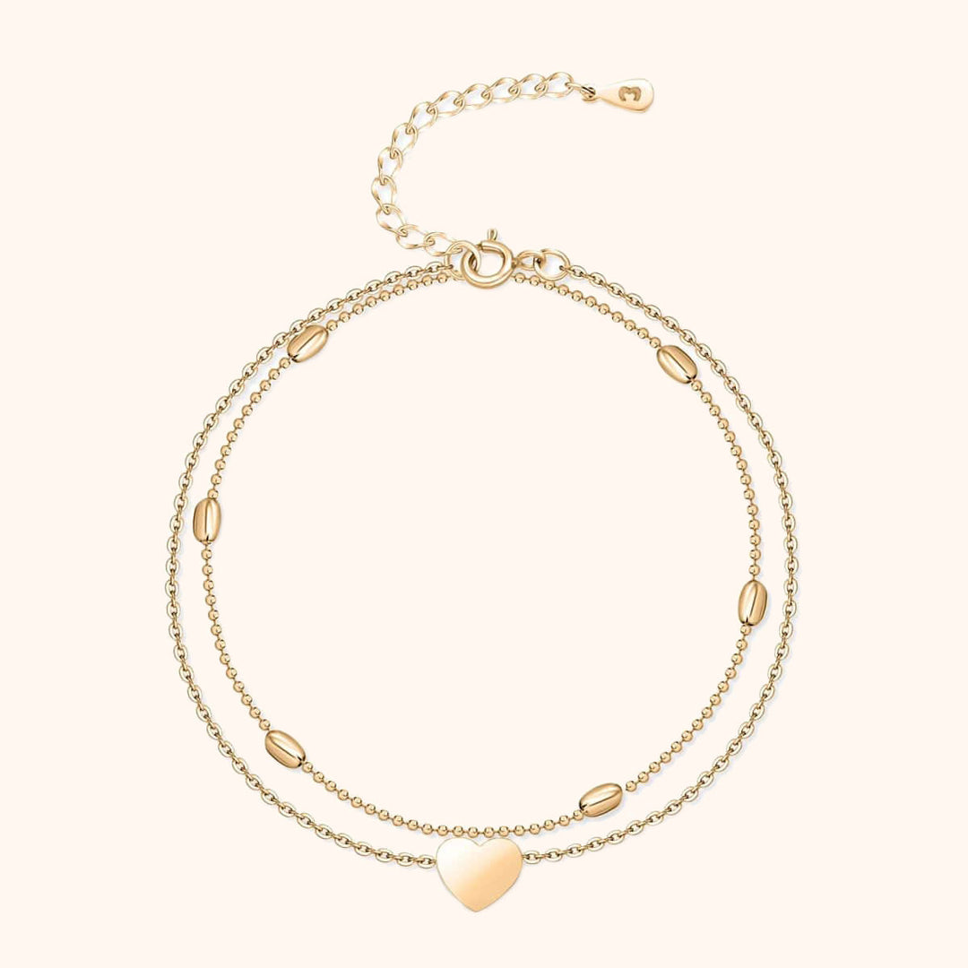 Zweireihiges goldfarbenes Armband mit Herzanhänger und ovalen Details, verstellbar.
