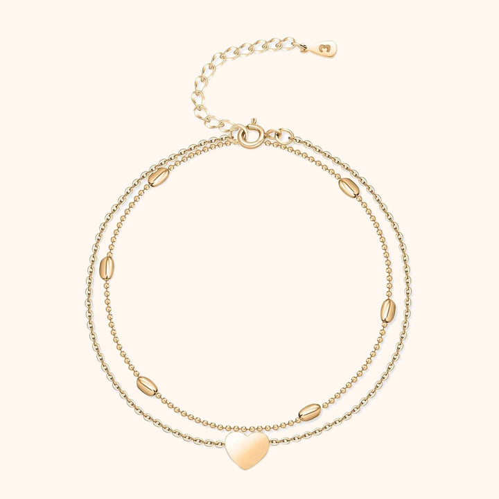 Zweireihiges goldfarbenes Armband mit Herzanhänger und ovalen Details, verstellbar.