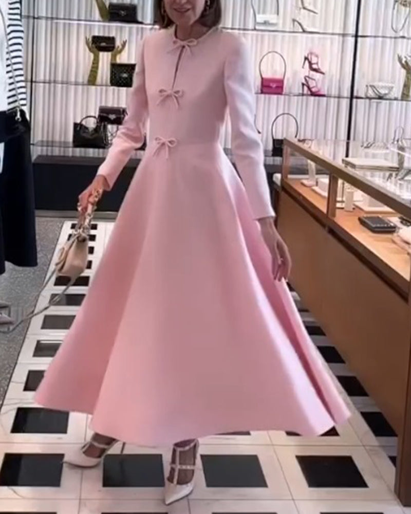 Elegantes rosa Abendkleid, langärmelig, mit Schleifen, ausgestellt, in Boutique-Umgebung.