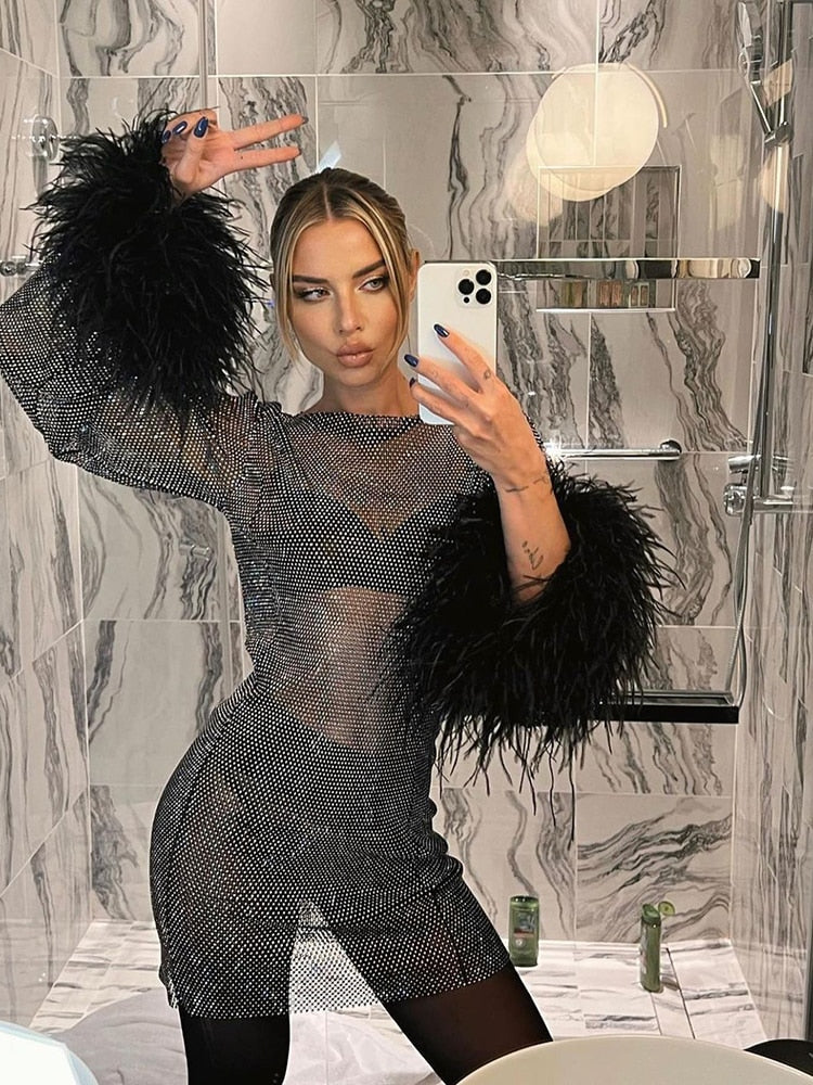 Frau in schwarzem Netzkleid mit Federärmeln, Selfie im Marmor-Badezimmer.