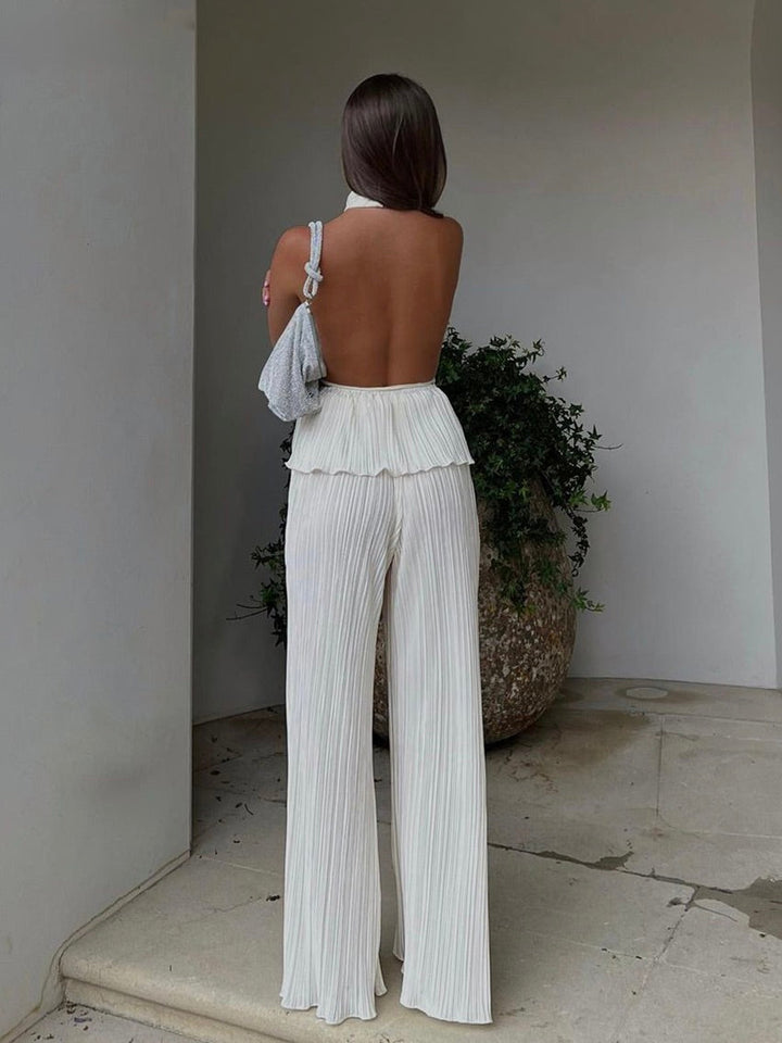 Frau in weißem, rückenfreiem Jumpsuit mit Plissee, graue Tasche, elegantes Sommeroutfit.