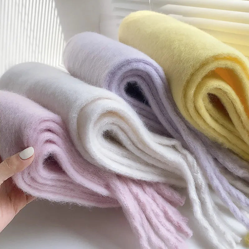 Drei weiche Wollschals in Pastellfarben: Rosa, Weiß, Gelb, auf einem Tisch drapiert.