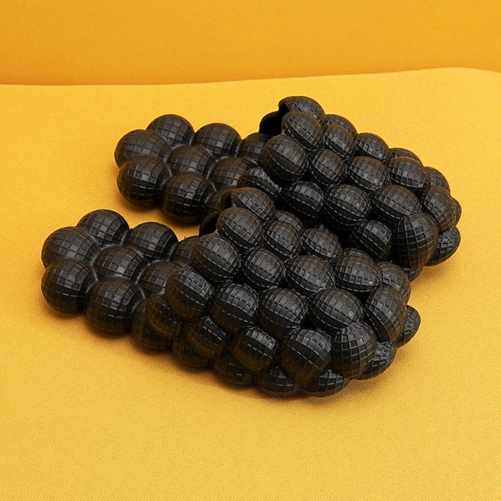Schwarze, gepolsterte Massagesandalen auf gelbem Hintergrund, rutschfest, ergonomisch.