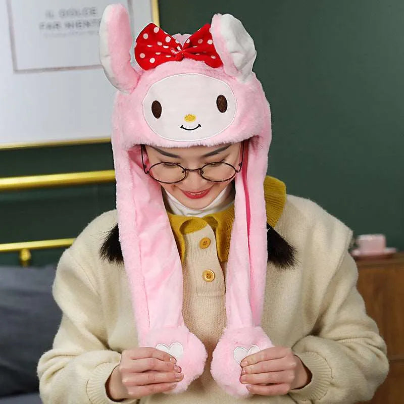 Frau mit rosa Plüsch-Hasenmütze, roter Schleife, Brille, gelbem Pullover, lächelnd.