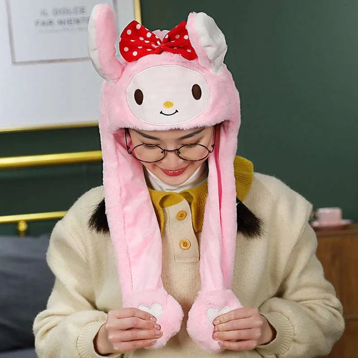 Frau mit rosa Plüsch-Hasenmütze, roter Schleife, Brille, gelbem Pullover, lächelnd.