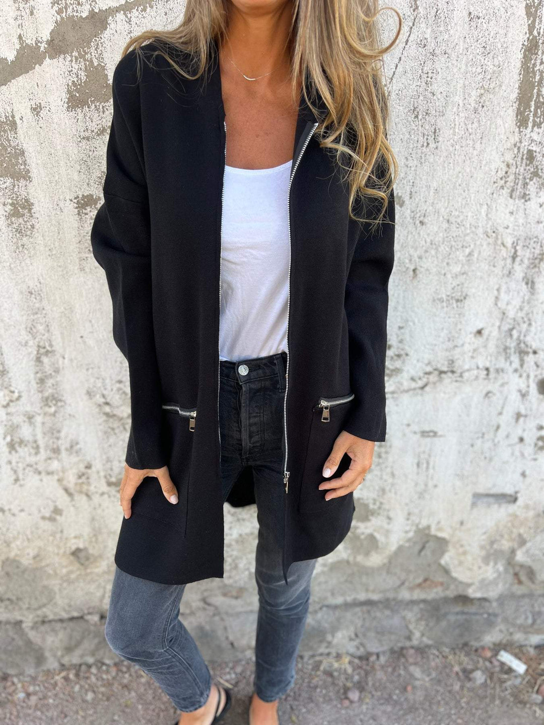 Frau trägt schwarze, halblange Kapuzenjacke mit Reißverschluss, lässiger Stil, modisch.