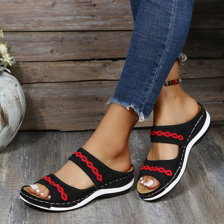 Schwarze Damen-Sandalen mit rotem Muster, bequem, lässig, ideal für Sommer, Holz-Hintergrund.
