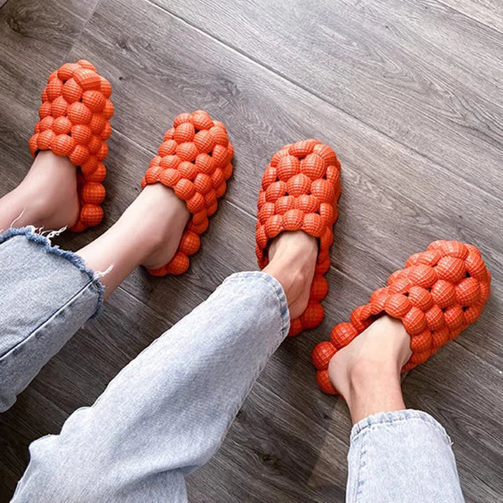 Orange Massageslipper aus Kunststoff auf Holzboden, bequem, modern, unisex, für Zuhause.